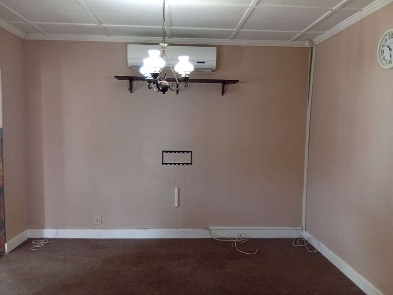 A living room space featuring carpet flooring, a wall-mounted air conditioning unit, and a TV bracket, presenting a blank canvas for interior updates.