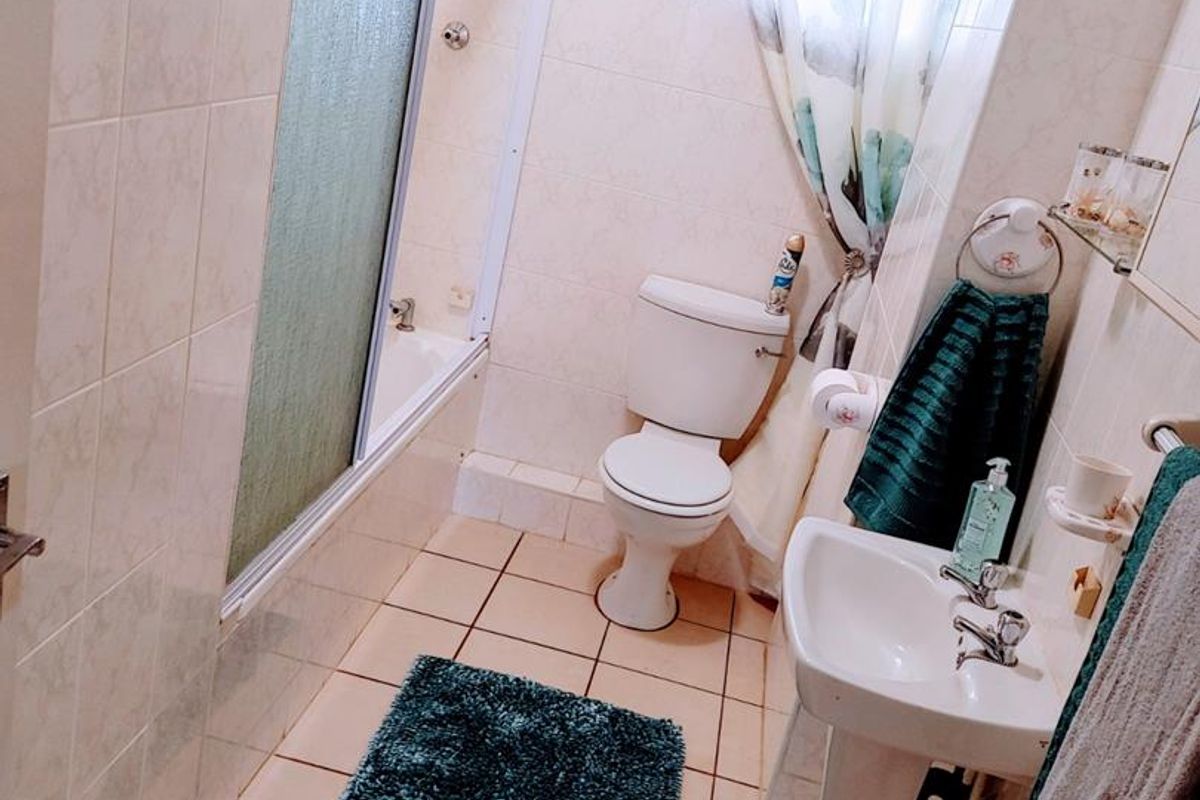 A functional bathroom featuring a pedestal basin, a toilet, and a shower-over-bath combination with sliding glass doors and tiled finishes.