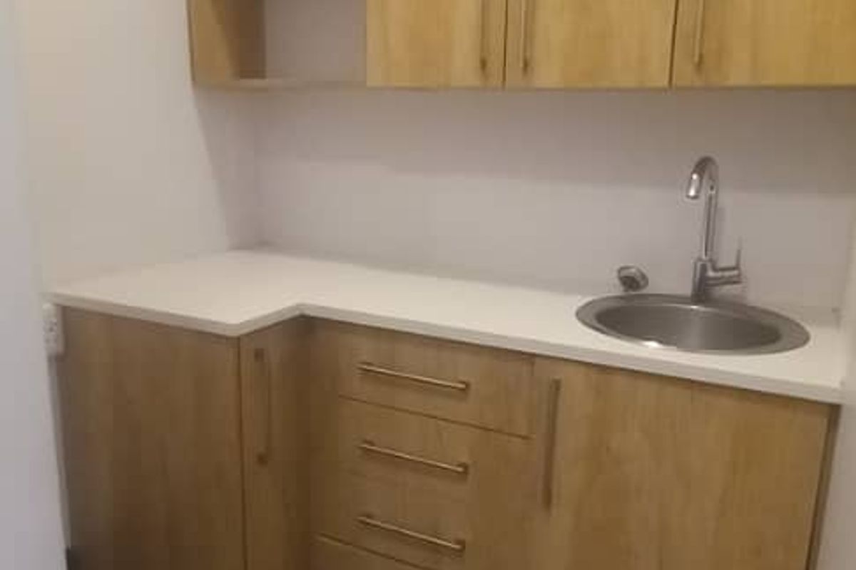 A clean and modern scullery or kitchenette area featuring light wood-finish cabinetry, a white countertop, and a stainless steel sink.