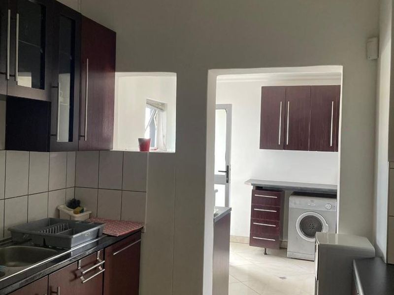 A functional kitchen featuring dark wood cabinetry, tiled backsplash, and a connected laundry area with built-in storage and tiled flooring throughout.