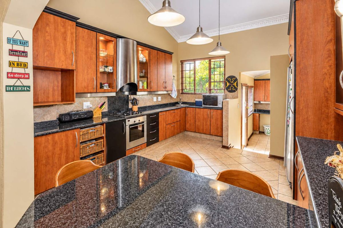 Spacious kitchen featuring warm wood cabinetry, granite countertops, built-in appliances, and a breakfast nook, with an adjoining scullery area.