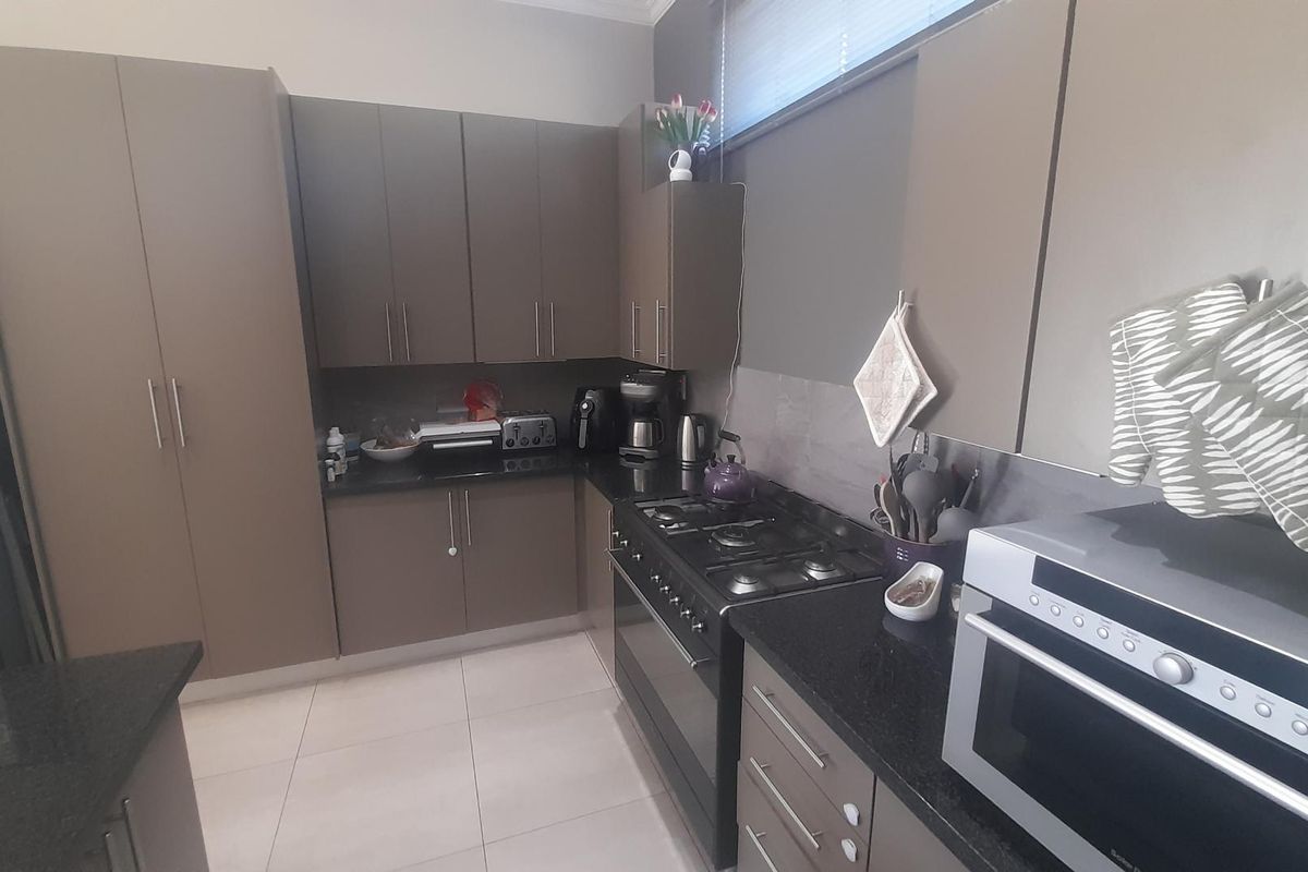 Modern kitchen featuring dark cabinetry, granite countertops, a gas hob, and built-in oven with tiled flooring.