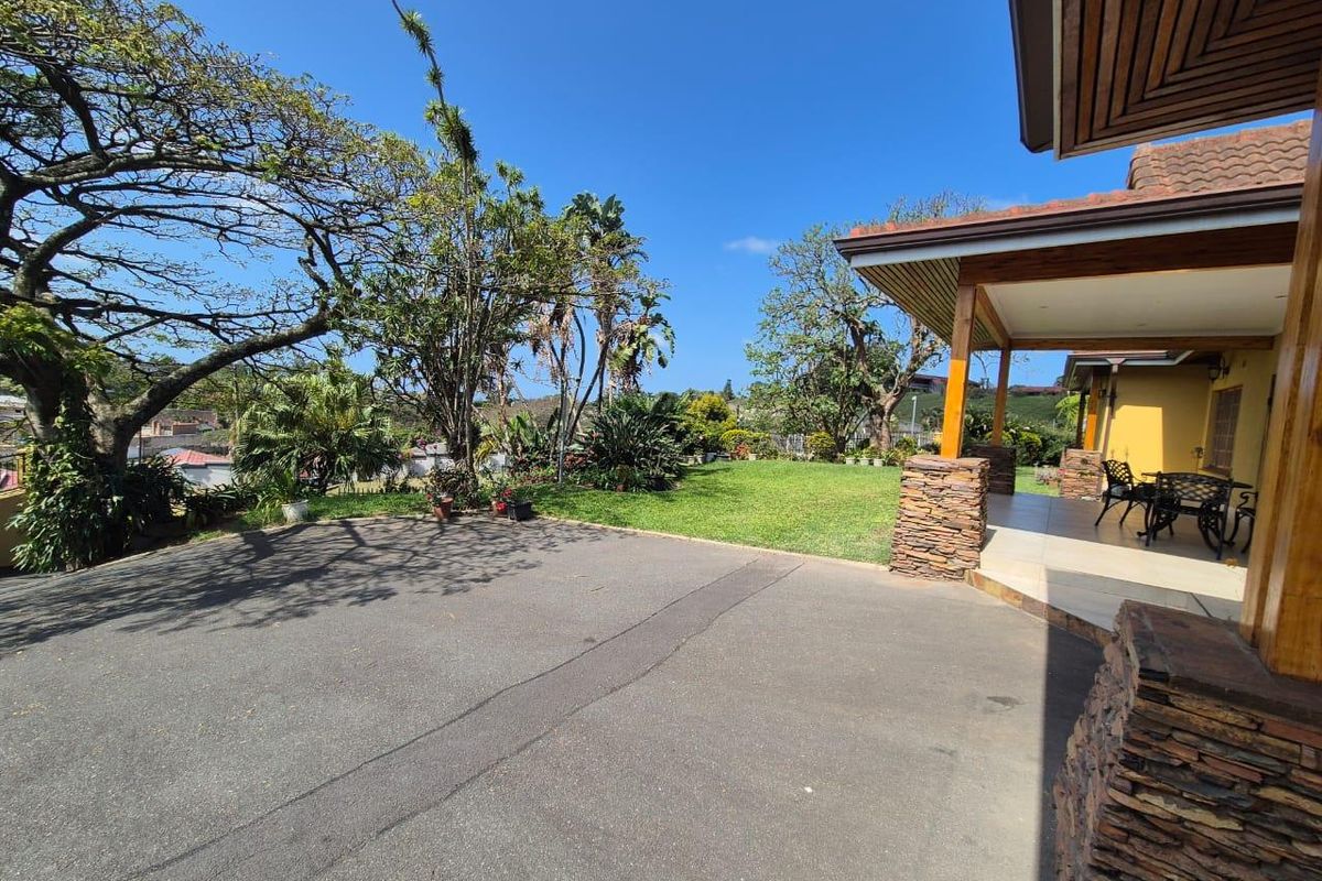A spacious rear exterior featuring a covered patio with stone-clad pillars, overlooking a well-maintained lawn and mature garden area.