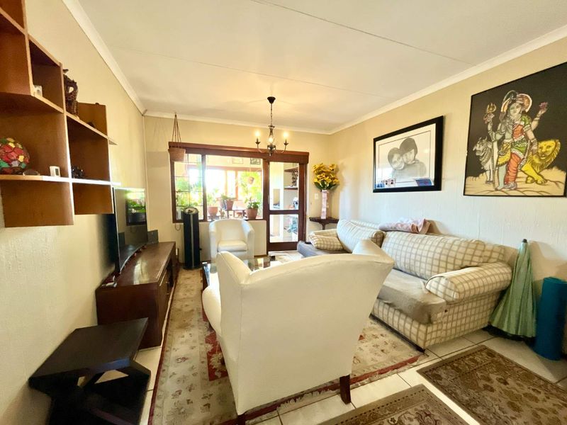 A comfortable living room featuring tiled flooring, a classic chandelier, and timber-framed glass doors leading to an adjacent space.