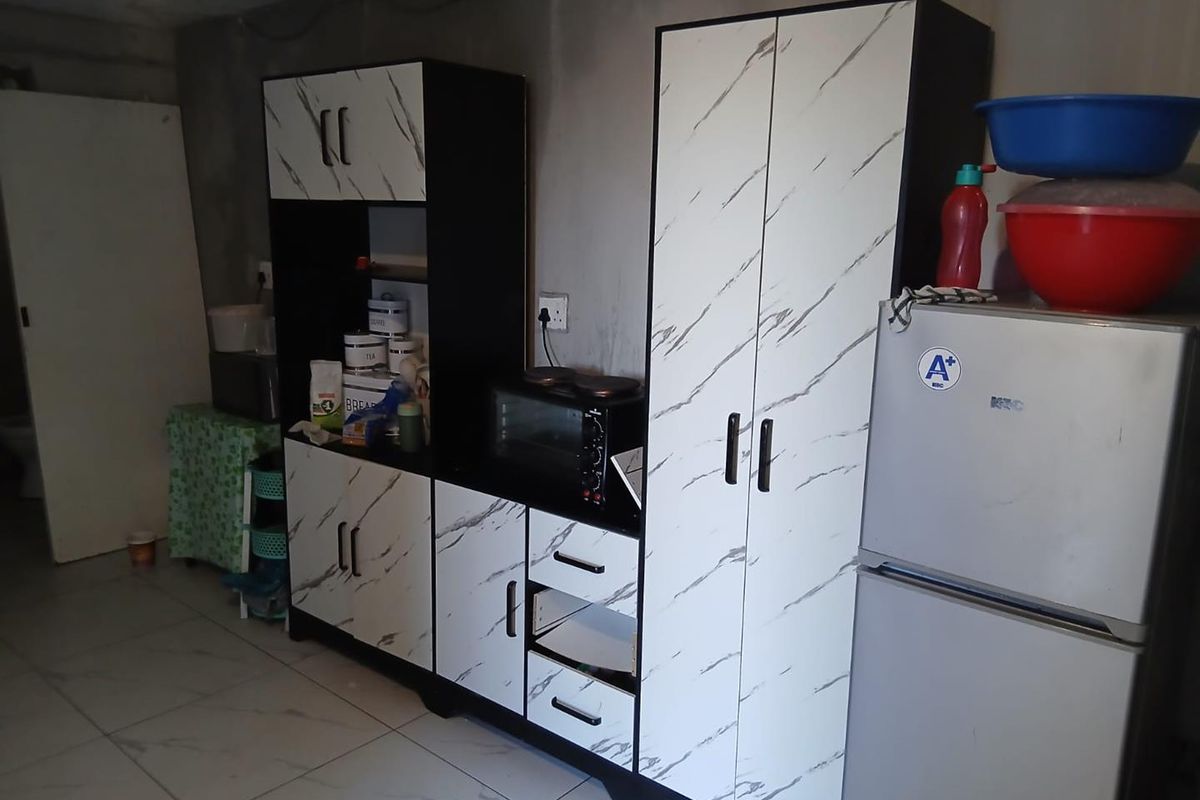 A kitchen area featuring modern marble-effect cabinetry and tiled flooring, set against unfinished raw concrete walls with exposed wiring.