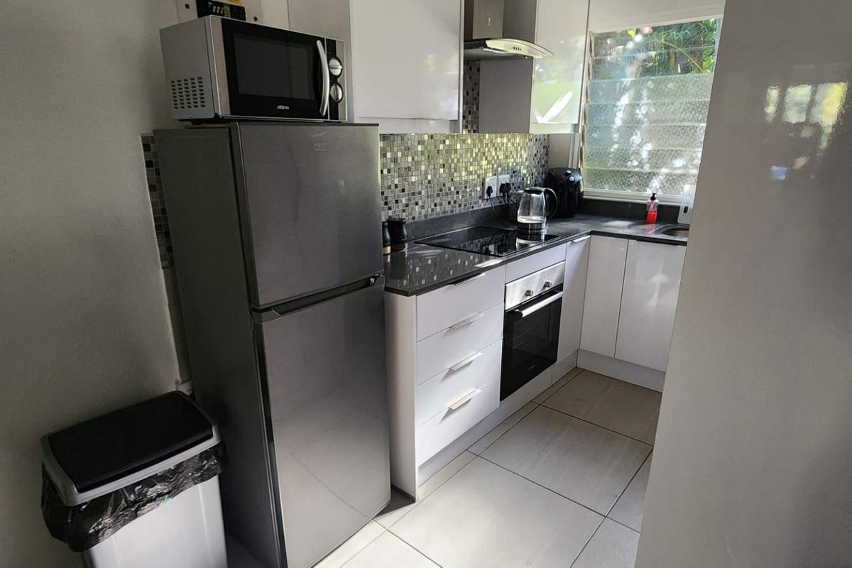 Compact modern kitchen featuring white cabinetry, dark stone countertops, a mosaic tile backsplash, built-in oven, and hob.