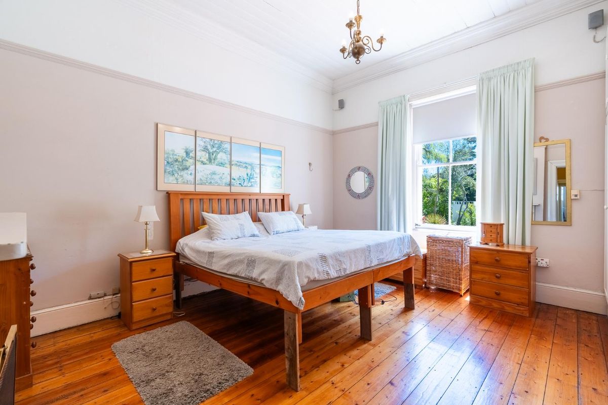 Spacious bedroom featuring original timber flooring, high ceilings with coved detailing, and a large sash window providing natural light.