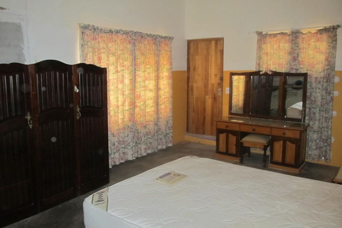 A bedroom featuring a wooden door, dual windows with curtains, and basic wall finishes, providing a functional space for rest.