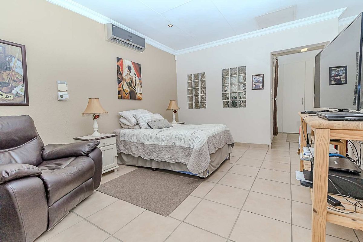 A bedroom featuring tiled flooring, cove cornicing, and glass block windows, equipped with a wall-mounted air conditioning unit.