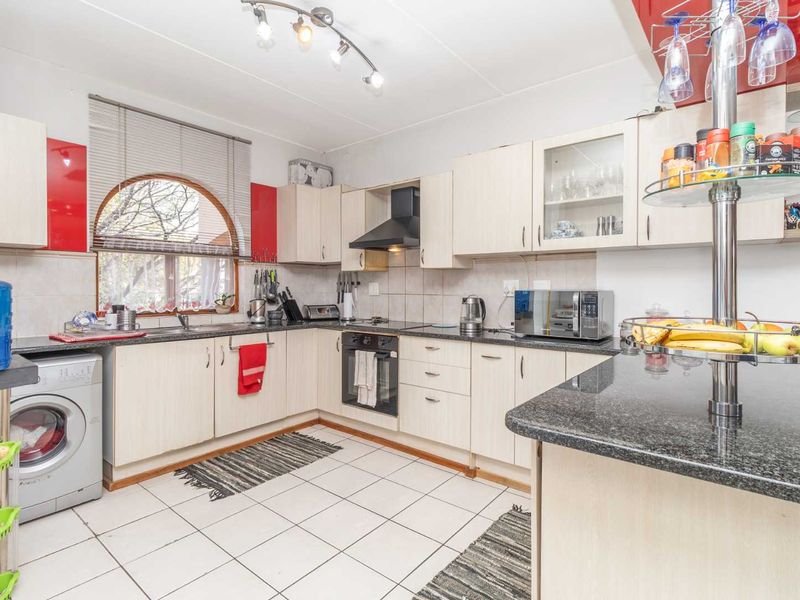 Functional kitchen featuring light-toned cabinetry, granite countertops, integrated oven and hob, tiled flooring, and a distinctive arched window providing natural light.
