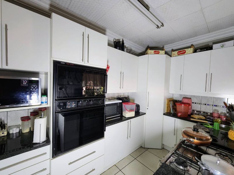 A functional kitchen featuring white built-in cabinetry, granite countertops, a built-in oven, and a gas hob, with tiled flooring throughout.