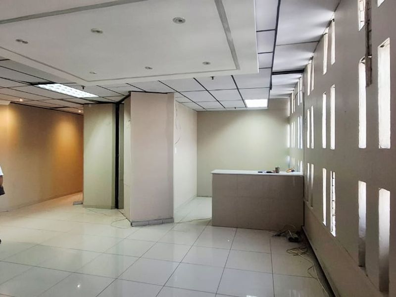 Spacious open-plan office area featuring a built-in reception counter, tiled flooring, and a suspended ceiling with recessed lighting.