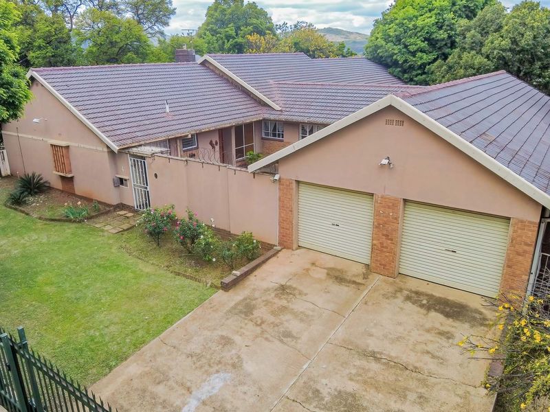 Elevated view of a residential property featuring a double garage, concrete driveway, and tiled roof, set within a landscaped garden with perimeter fencing.