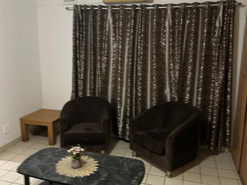 A living room area featuring tiled flooring, a wall-mounted air conditioning unit, and window curtains.