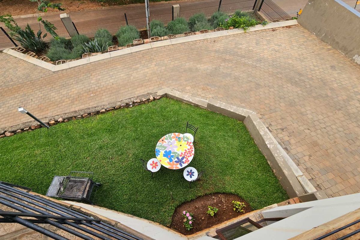 An elevated view of a private garden area featuring a paved driveway, manicured lawn, and retaining walls.