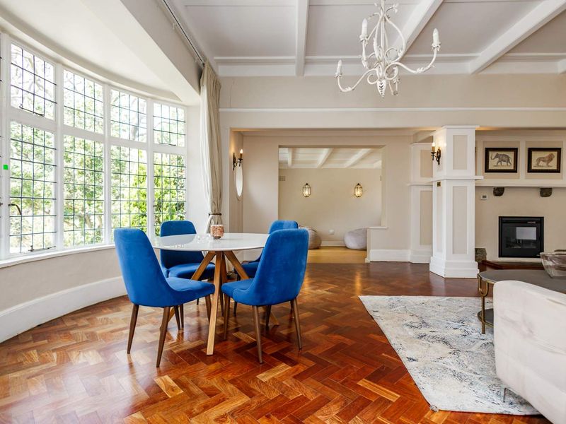Spacious open-plan living and dining area featuring elegant herringbone parquet flooring, a coffered ceiling, and a classic leaded glass bay window.
