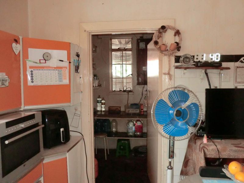 A view into a functional scullery or utility area featuring built-in cabinetry and a window with security bars, showing signs of wear.
