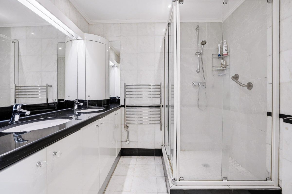 Modern bathroom featuring a double vanity with black granite countertops, integrated cabinetry, a glass-enclosed shower, and a heated towel rail.