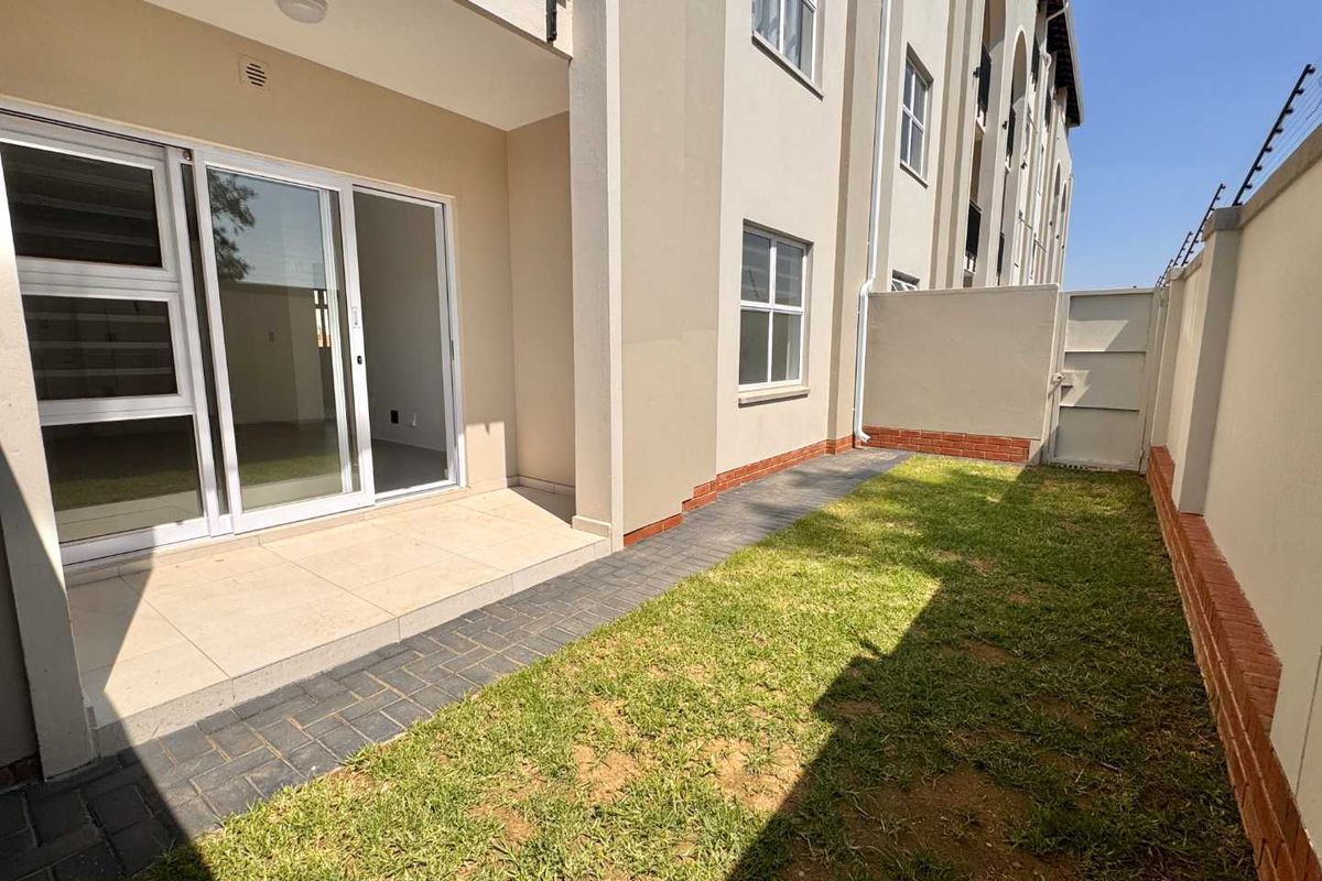 A private rear garden area featuring a tiled patio, paved walkway, and a secure boundary wall with a pedestrian gate.