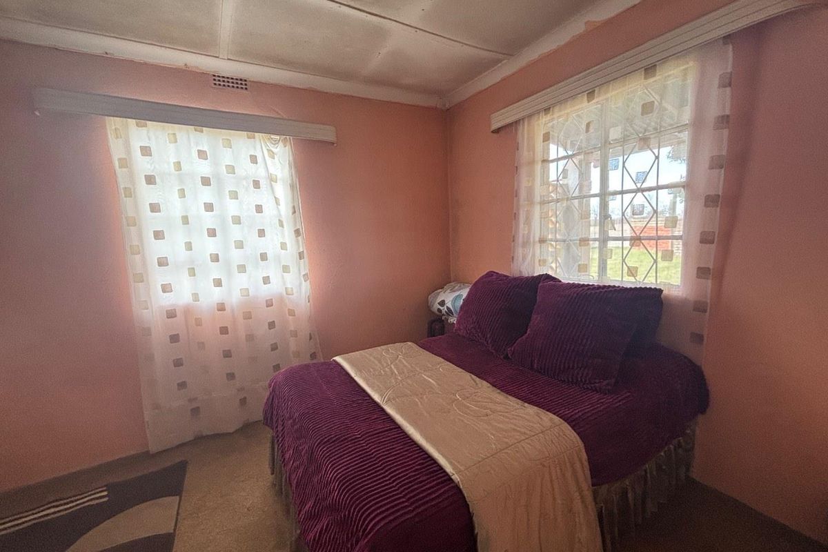 A bedroom featuring two windows with security bars, standard ceiling tiles, and carpeted flooring, requiring cosmetic updates to modernize the space.