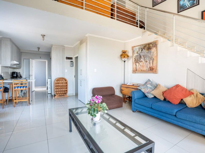 Open-plan living area featuring a modern kitchen with island, tiled flooring, and a staircase leading to a mezzanine level.