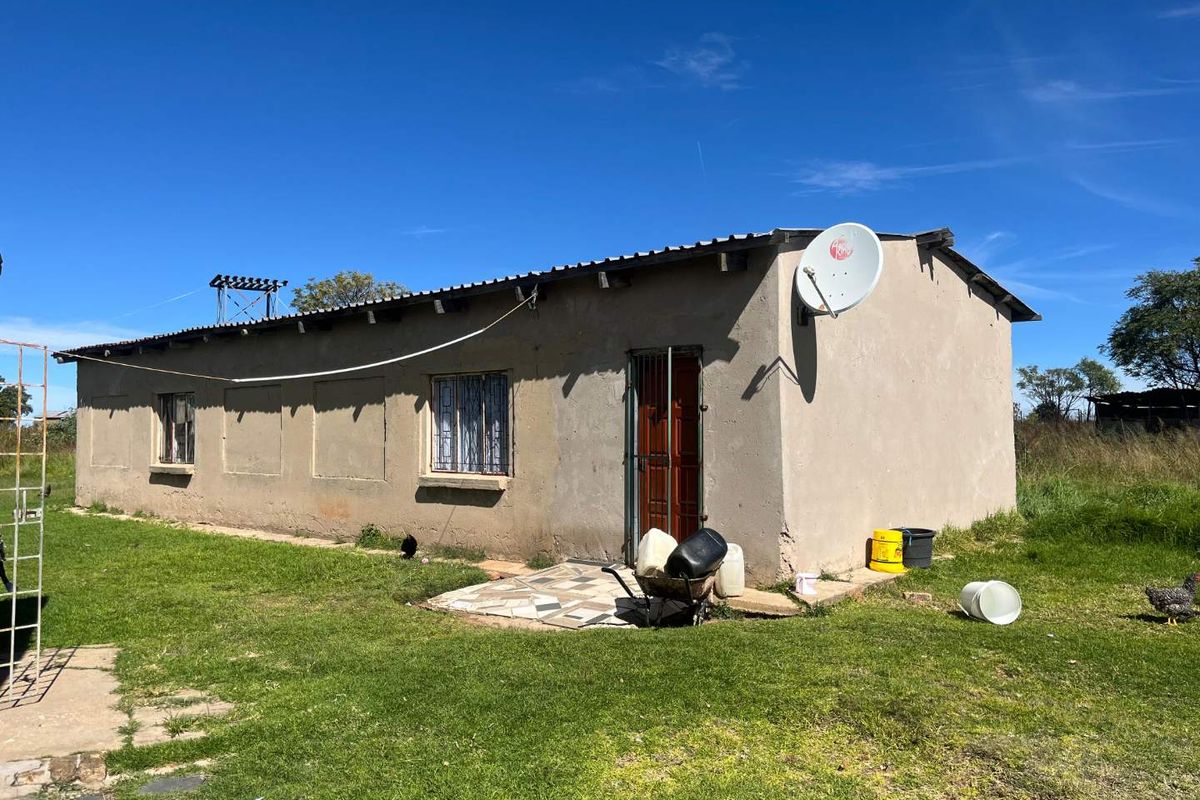 Exterior view of a single-story farm dwelling featuring a simple plaster finish, metal roof, and security gate entrance.