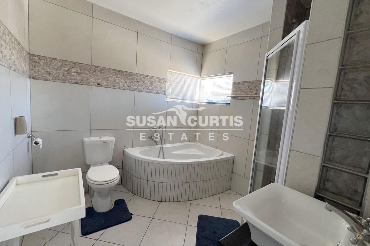 A functional bathroom featuring a corner bathtub, a separate shower enclosure, a toilet, and a vanity basin with neutral wall and floor tiling.