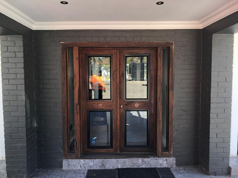 A modern office entrance featuring double timber doors with glass panels, set within a dark painted brick facade and stone threshold.