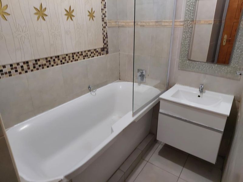 A functional bathroom featuring a bathtub with a glass shower screen, a wall-mounted vanity with a basin, and decorative tiled wall accents.