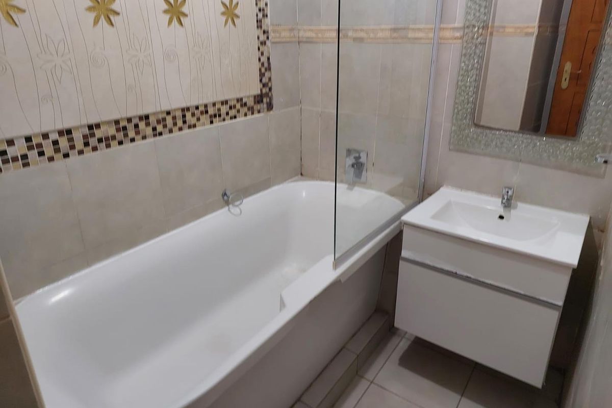 A functional bathroom featuring a bathtub with a glass shower screen, a wall-mounted vanity with a basin, and decorative tiled wall accents.