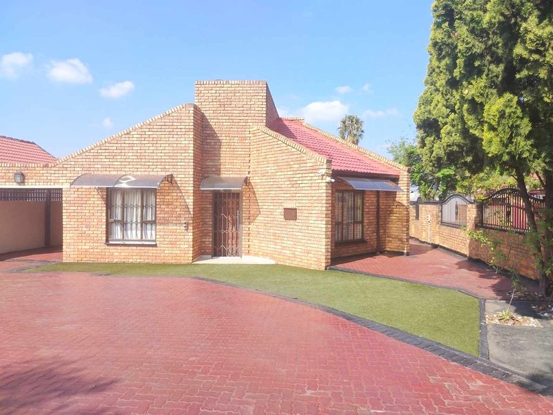 Front view of a well-maintained face brick house featuring a paved driveway, artificial lawn, and secure entrance with security gate.