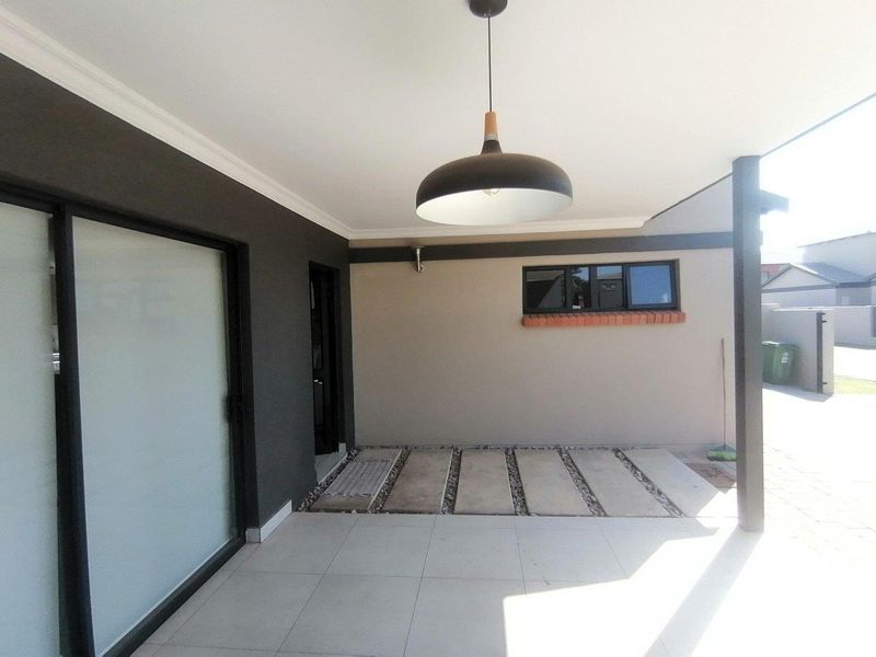 A covered patio area featuring tiled flooring, concrete pavers, and a modern pendant light, providing a clean outdoor space for relaxation.