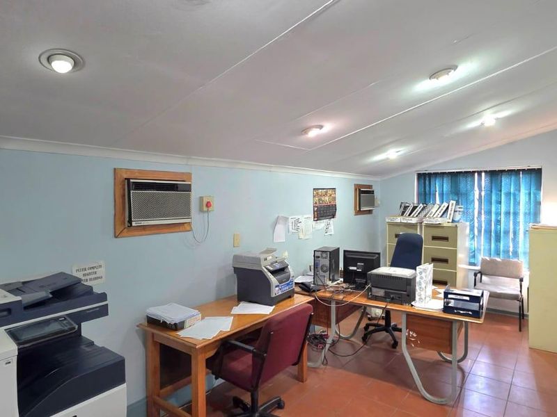 A functional office space featuring tiled flooring, recessed ceiling lighting, and a window-mounted air conditioning unit.