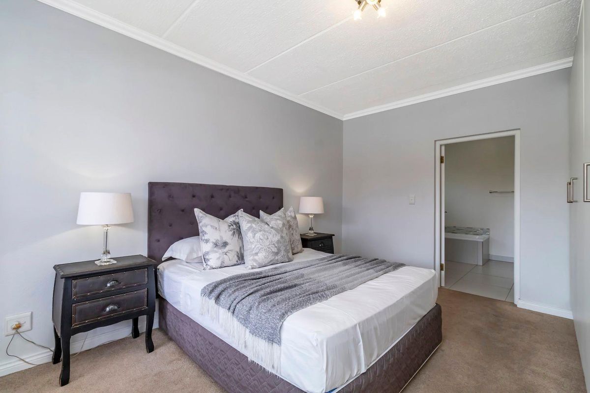 A well-lit bedroom featuring neutral wall tones, carpeted flooring, and an en-suite bathroom access point.