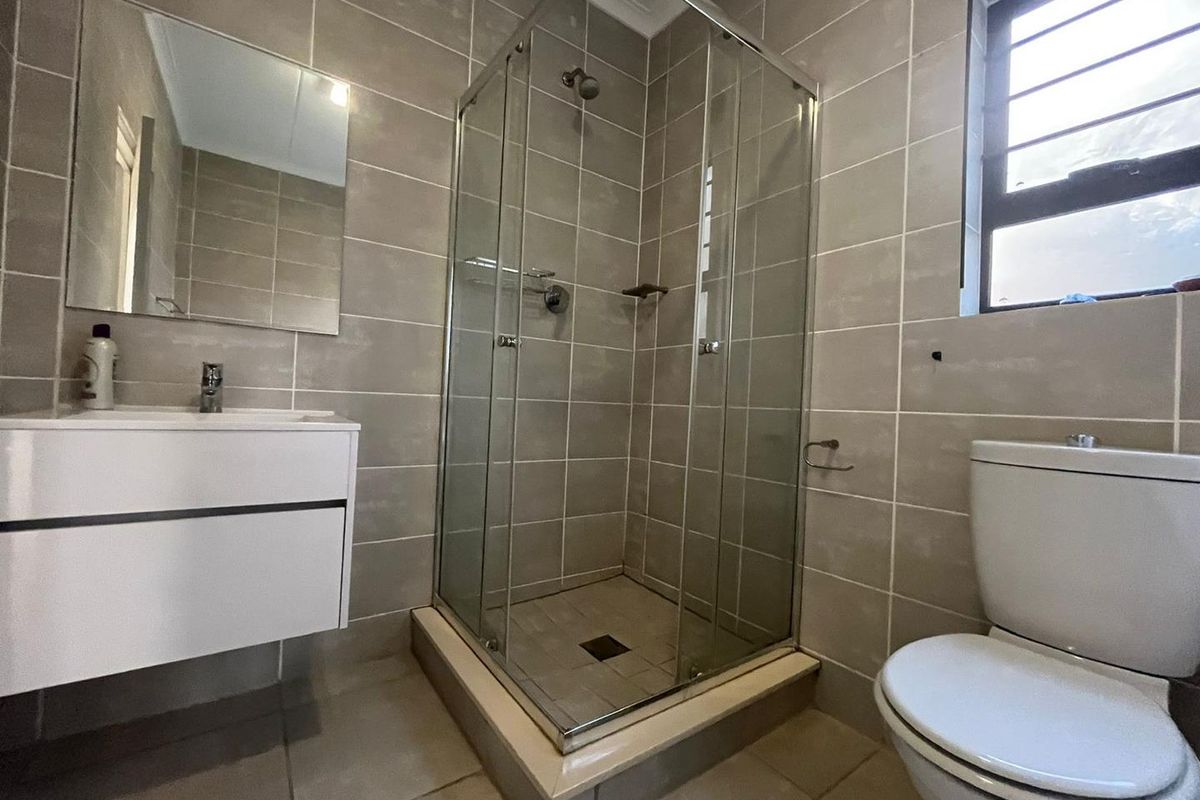 A modern bathroom featuring a glass shower enclosure, wall-mounted vanity, and neutral tiled finishes throughout.