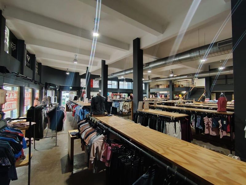 Spacious open-plan retail floor featuring industrial-style exposed ducting, concrete flooring, structural columns, and a mezzanine level accessed by a staircase.