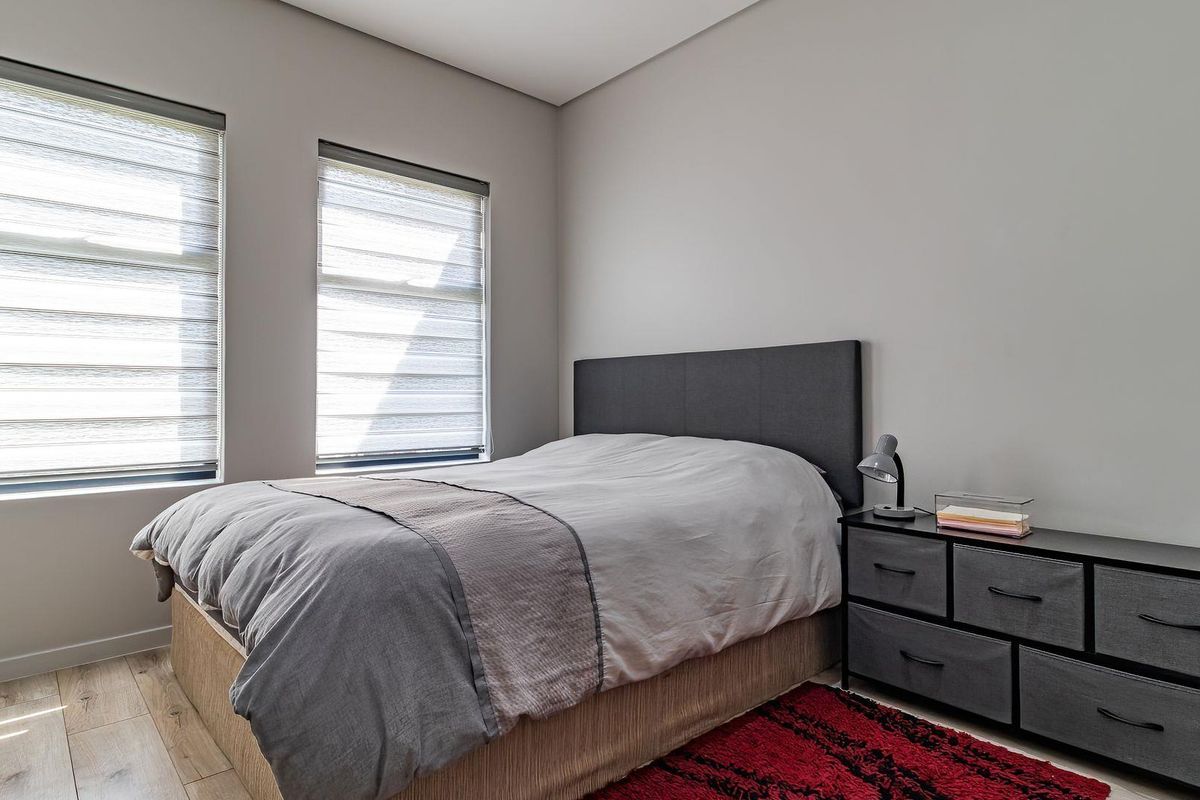 A well-maintained bedroom featuring neutral wall tones, modern laminate flooring, and dual windows fitted with contemporary roller blinds.