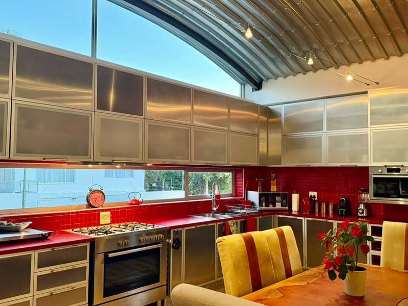 Modern kitchen featuring stainless steel cabinetry, red tiled backsplash, gas cooktop, built-in oven, and a unique curved metal ceiling with clerestory windows.