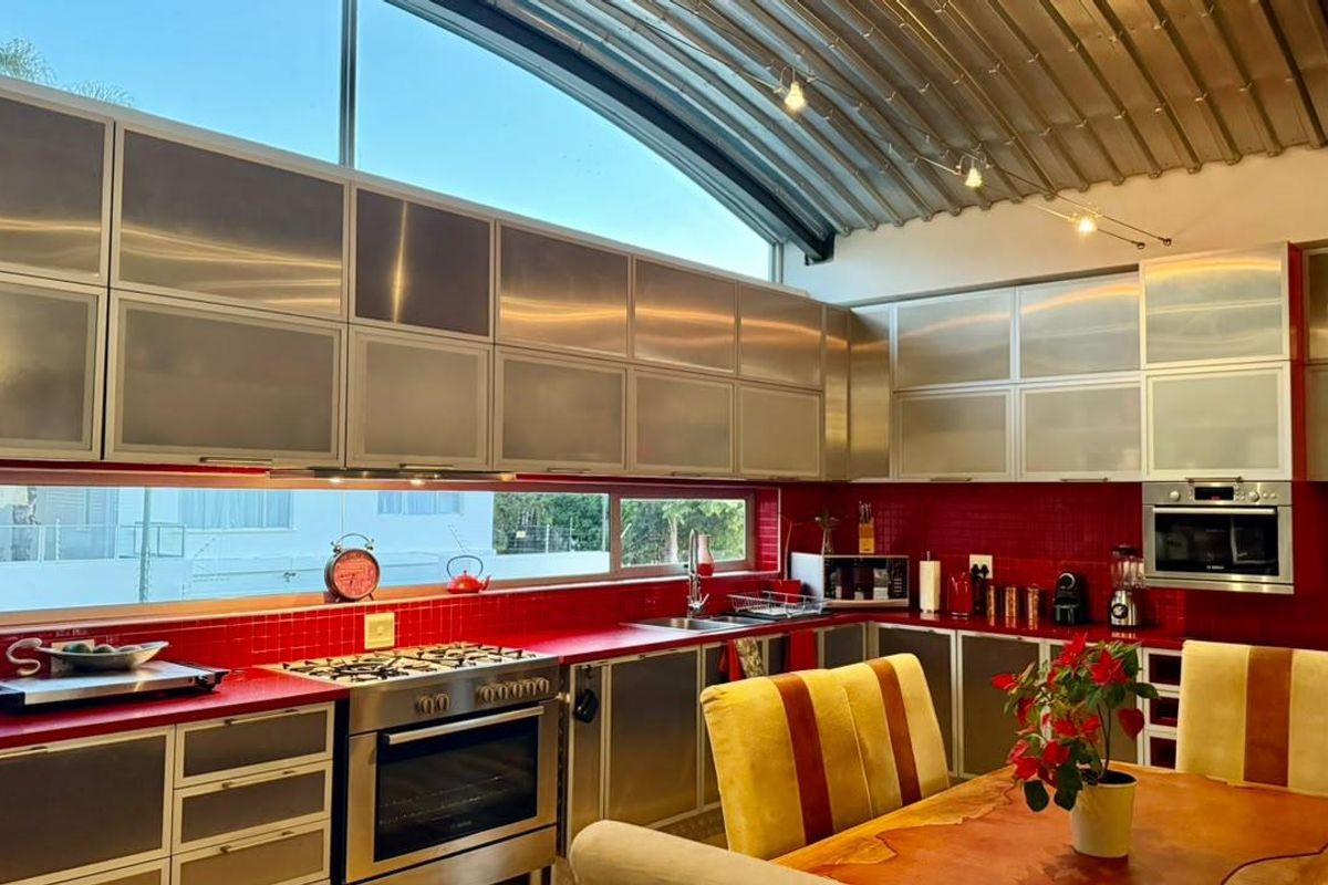 Modern kitchen featuring stainless steel cabinetry, red tiled backsplash, gas cooktop, built-in oven, and a unique curved metal ceiling with clerestory windows.