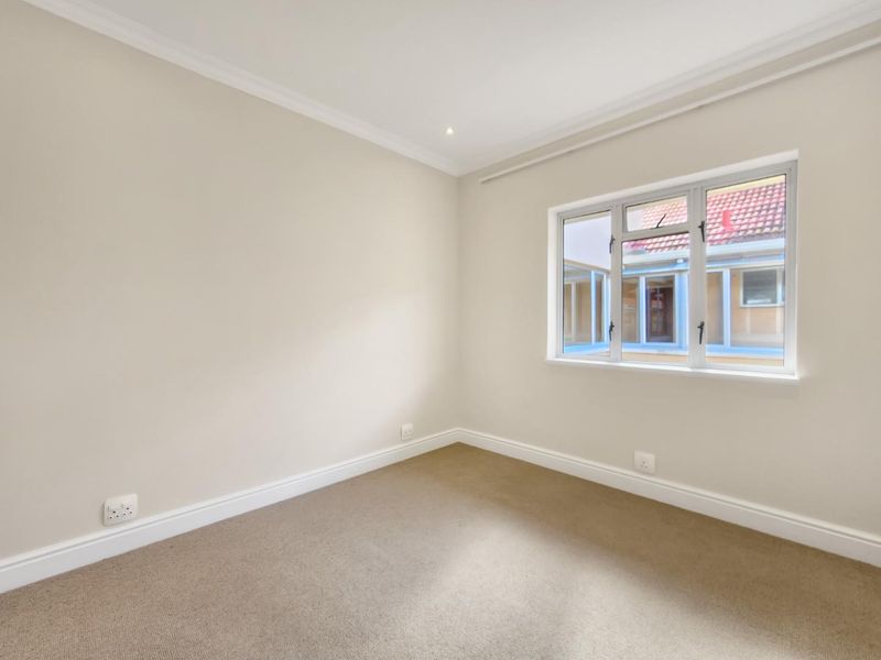A clean, empty bedroom featuring neutral wall tones, carpeted flooring, and a window providing natural light.
