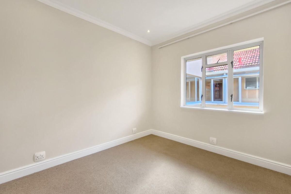 A clean, empty bedroom featuring neutral wall tones, carpeted flooring, and a window providing natural light.