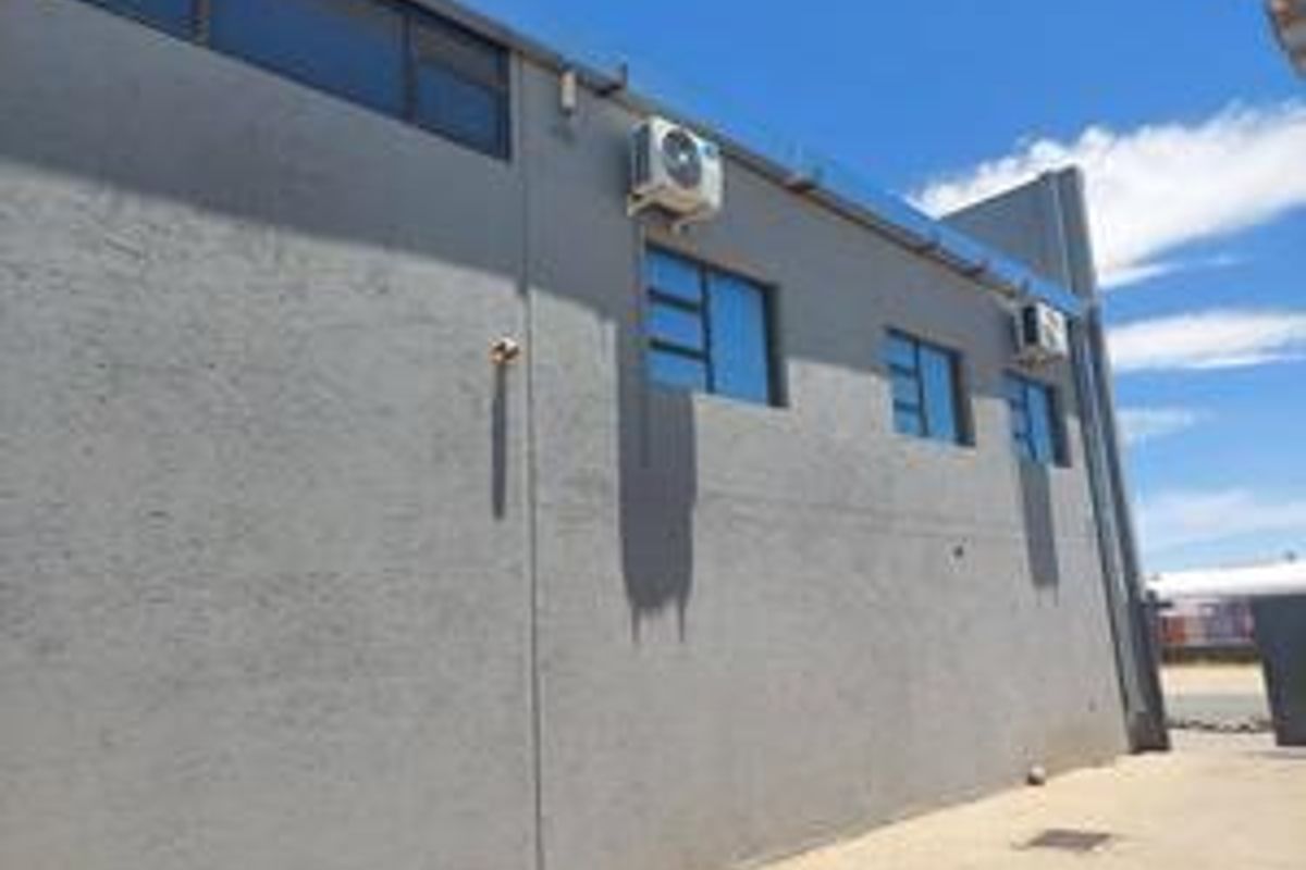 Exterior view of the industrial property featuring a grey rendered facade, multiple windows, and wall-mounted air conditioning units.