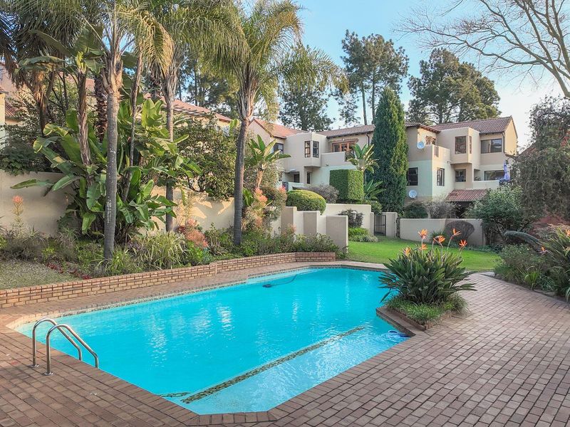 A well-maintained communal pool area featuring brick paving, established landscaping, and views of the surrounding apartment complex buildings.