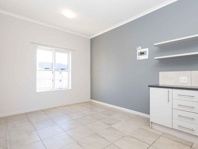 An open-plan living area featuring tiled flooring, a compact kitchen section with built-in cabinetry, and floating shelves against a grey accent wall.