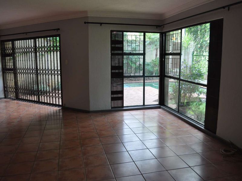 Spacious living area featuring ceramic tile flooring, large windows with garden views, and integrated metal security gates, offering a bright and open layout.