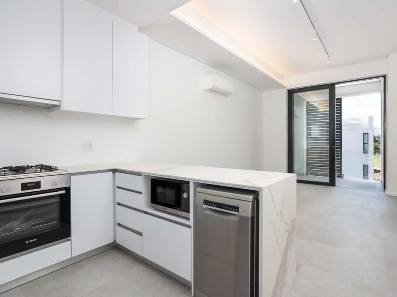 Modern open-plan kitchen featuring sleek white cabinetry, stone countertops, integrated appliances, and direct access to a private balcony through sliding glass doors.