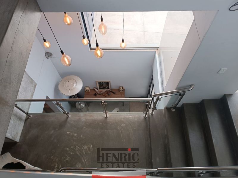 A modern staircase featuring polished concrete steps, a sleek stainless steel and glass balustrade, and a large skylight providing natural light.