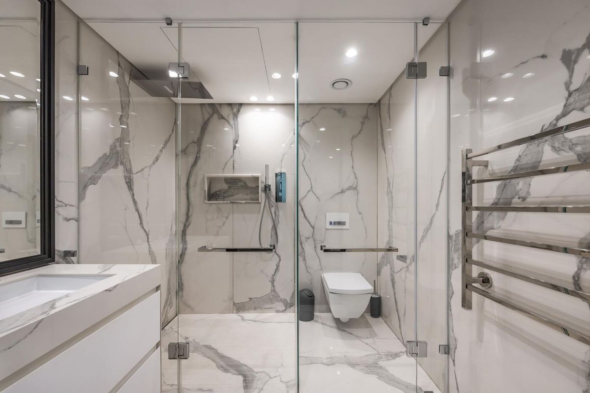 Modern luxury bathroom featuring floor-to-ceiling marble tiling, a frameless glass shower enclosure, wall-mounted toilet, and a sleek vanity with integrated basin.