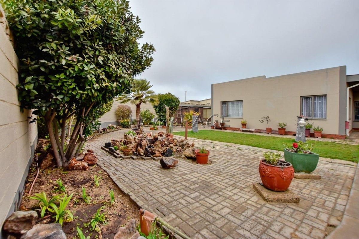 A rear garden area featuring a paved patio, a central rockery feature, and a lawn area adjacent to the house exterior.