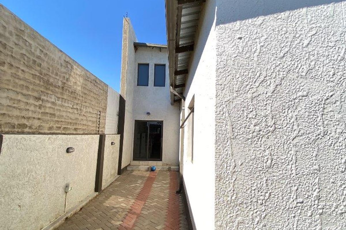 A narrow side passage featuring paved flooring, textured exterior walls, and a covered overhead structure leading toward the rear entrance.